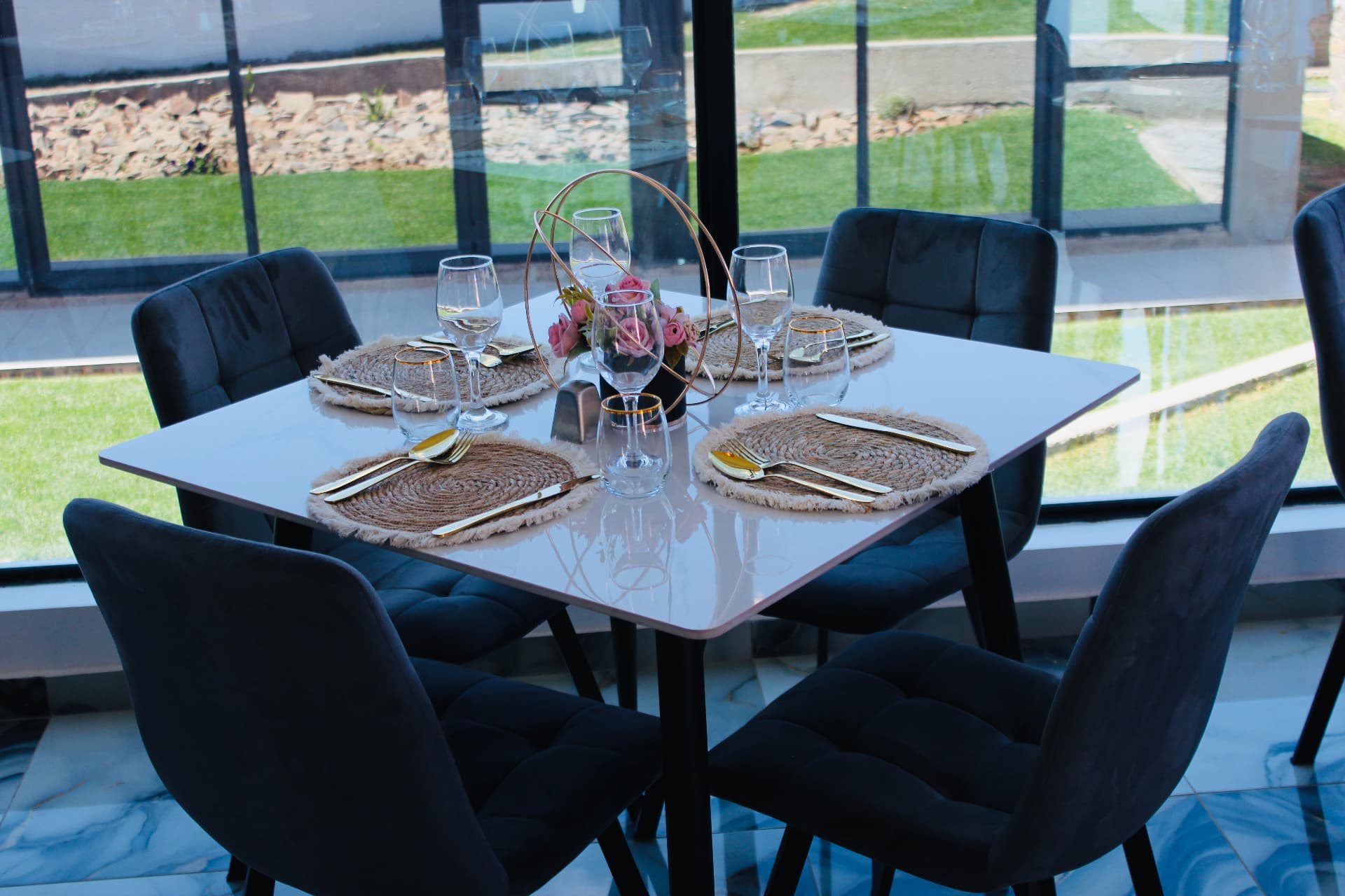 A table set with gold cutlery and fresh roses beside floor-to-ceiling windows